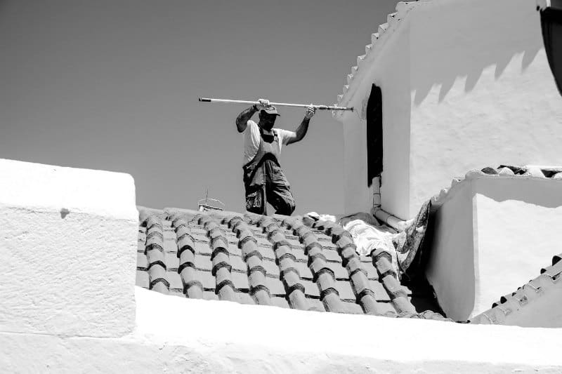 A local man applying white paint to a building exterior in Lindos