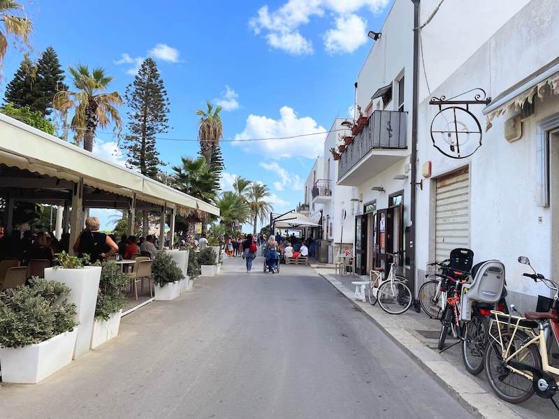 Main street by the beach in San Vito with cafe seating on the left.