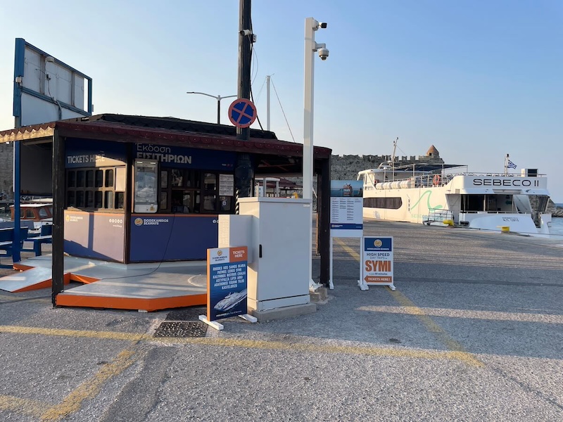 A small sheltered wooden kiosk with picnic benches and information boards, with the Sebeco II ferry in the background.