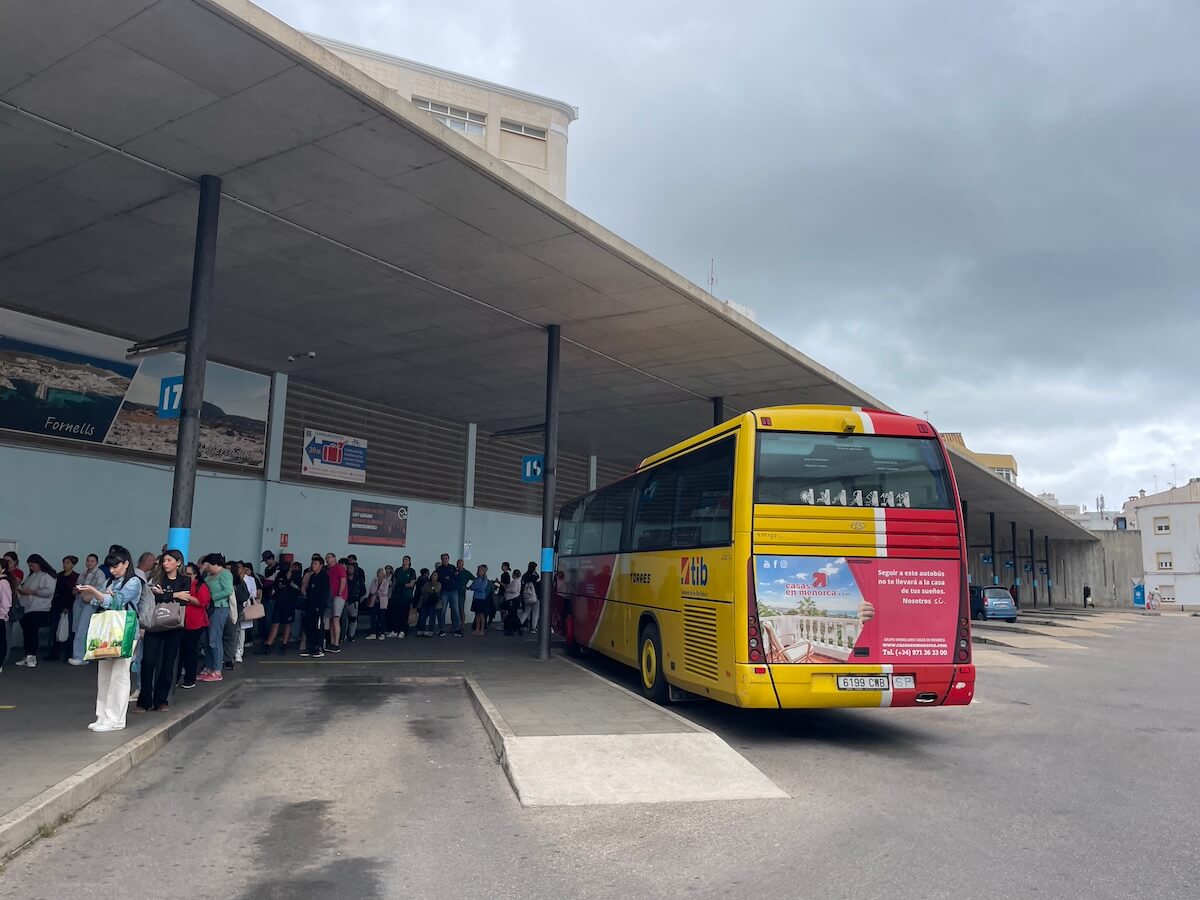 Red and yellow TMSA coach in Mahon bus station, with a queue of passengers waiting to get on.