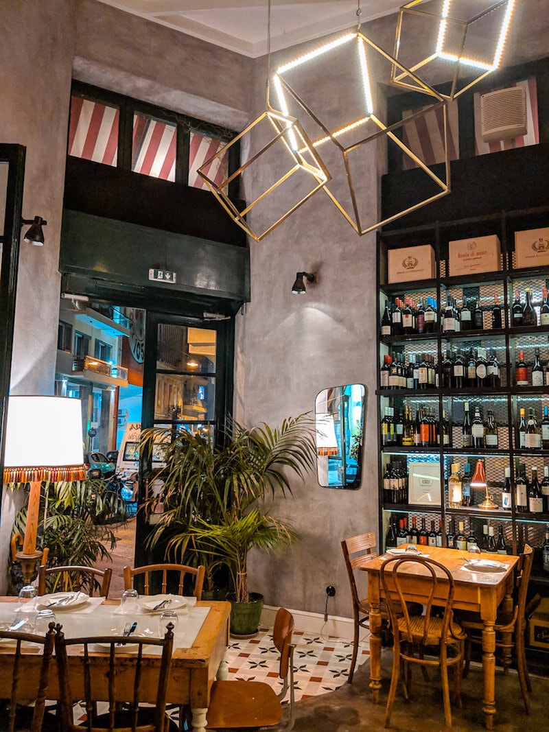 Interior of Zampano wine bar with palm tree, empty tables, and stylish cubic lighting.