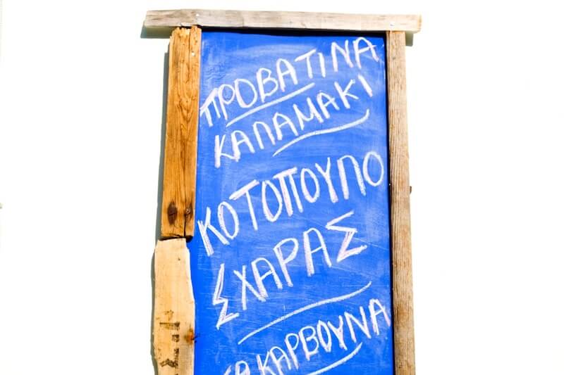 A bright blue menu board with items written in Greek.