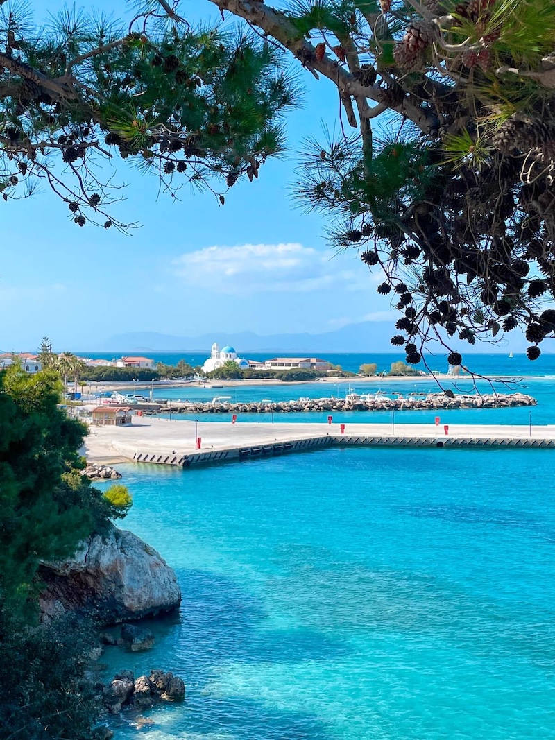 The Church of Agioi Anargyroi through the pine trees, surrounded by bright turquoise seas.
