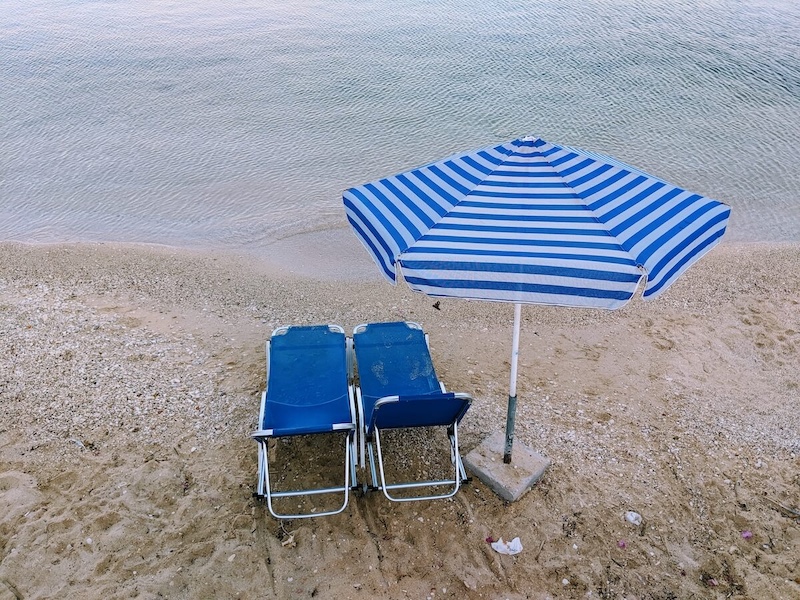 Sunloungers and a parasol on Agia Efimia's narrow beach, from the road.