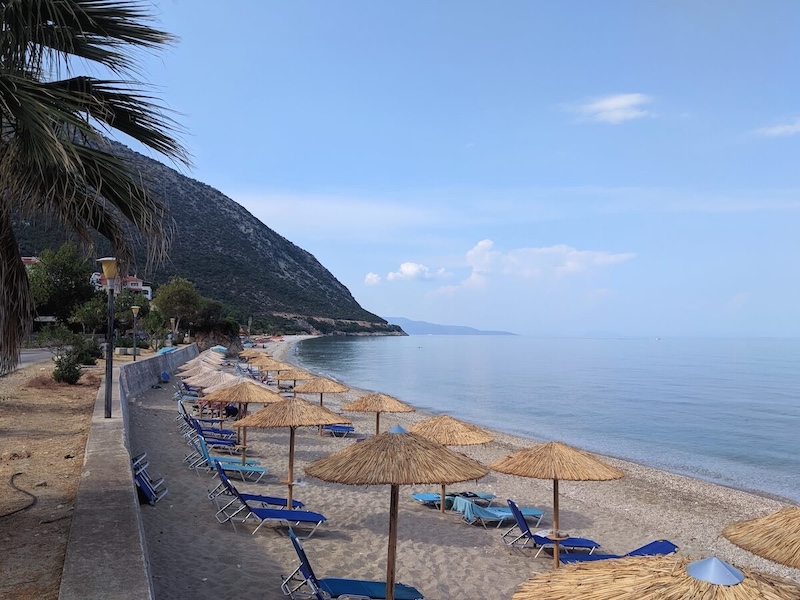 Empty sun loungers on the beach at Poros, with a flat calm sea.